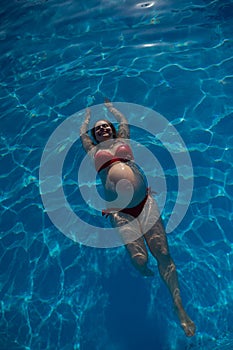 Top view of pregnant woman floating in pool in red bikini.