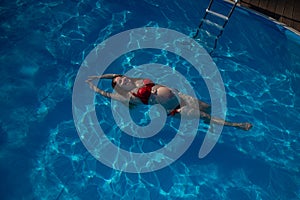 Top view of pregnant woman floating in pool in red bikini.