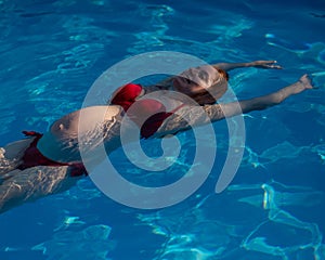 Top view of pregnant woman floating in pool in red bikini.