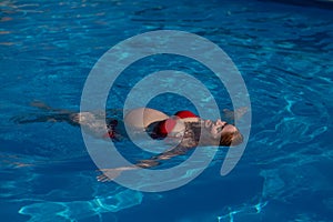 Top view of pregnant woman floating in pool in red bikini.