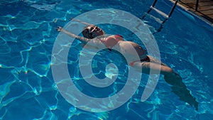 Top view of pregnant woman floating in pool in red bikini.