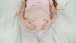 Top view of pregnant woman lying on hospital bed touching and stroking her big belly. Concept of pregnancy, preparing