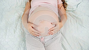 Top view of pregnant woman lying on hospital bed touching and stroking her big belly. Concept of pregnancy, preparing