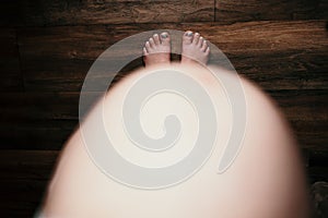 Top view of a pregnant woman's belly standing shoeless on the floor