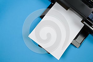 Top view of the printer and a blank sheet of a4 paper on a blue background