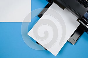 Top view of the printer and a blank sheet of a4 paper on a blue background.