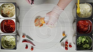 Top view of professional chef cooks a delicious burger at fast food restaurant. Female chef in gloves puts solt on