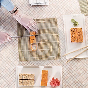 Top view of professional chef making and serving California sushi rolls in kitchen