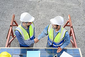 Top view of professional engineering people wearing helmets and safety vests meeting with solar photovoltaic panels handshake for