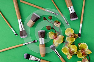 Top view of professional makeup brushes and decorative flower on the green background.Spring makeup trends