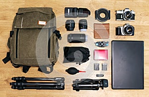 Top view of professional photography equipment over a wooden table cameras, lenses, tripods, backpack, laptop, accessories