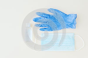 Top view of protective stuff, blue medical mask and glove, white bottle of sanitizer on light background.