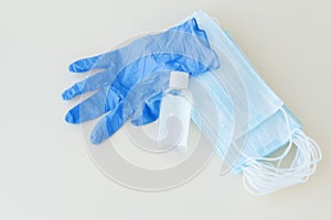 Top view of protective stuff, blue medical mask and glove, white bottle of sanitizer on light background.