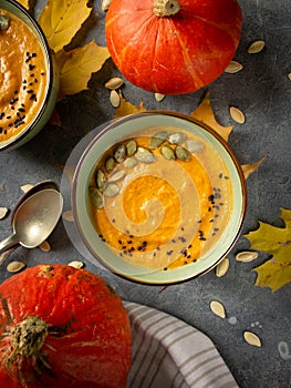 Top view of pumpkin soup bowl on cement surface with seeds, autumn leaves and pumpkins