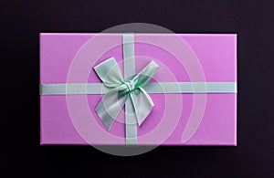 Top view purple present box with green bow on black background