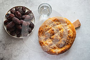 Top view of Ramadan Pide, medjoul date friuts and glass of water. Gray background