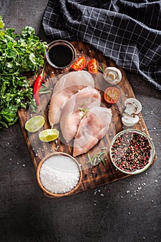 Top view on raw chicken breasts on a vitange cutting board on a dark metalic background, with various cooking