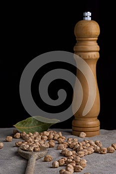 Top view of raw chickpeas, bay leaf, wooden spoon and pepper shaker on gray linen cloth