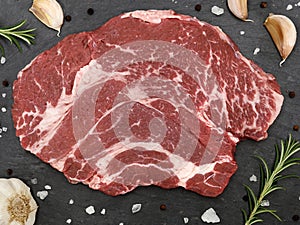 Top view of a raw chuck eye beef steak with herbs, spices and garlic on a slate serving board