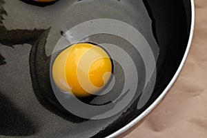 Top view on a raw egg with bright yellow yolk and transparent white with a clots in a black frying pan. The concept of  cooking