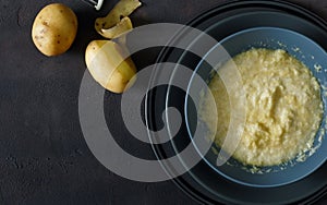 Raw grated potatoes for cooking potato pancakes on dark background