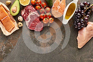 Top view of raw meat, fish and poultry near vegetables, fruits, eggs and olive oil on marble surface with copy space.