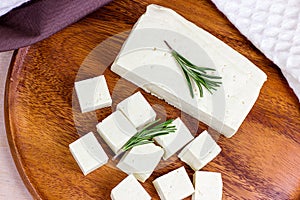 Top view of raw organic vegetarian tofu cubes with fresh rosemary on wooden background.