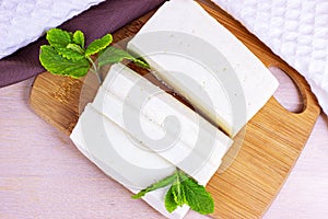 Top view of raw organic vegetarian tofu slices with fresh mint on wooden background.