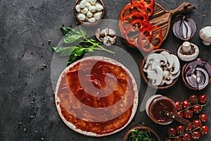 Top view of raw pizza dough with sauce and vegetables