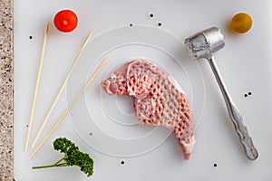 Top view of a raw pork steak next to a mallet on kitchen table