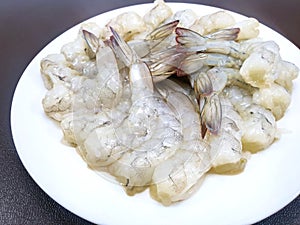 Top view raw prawns on white plate isolated on brown background