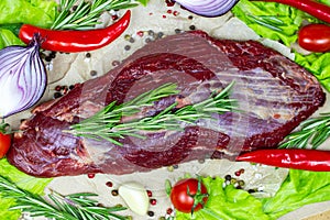 Top view of raw red beef meat with green rosemary and fresh vegetables on light wooden cutting board background.