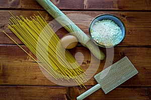 Top view of raw spaghetti with a rolling pin, a bowl of flour, and an egg on a wooden table