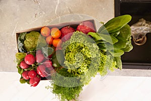 Top view of a recyclable cardboard box with fresh organic crop of fruits, vegetables and greens on the kitchen counter