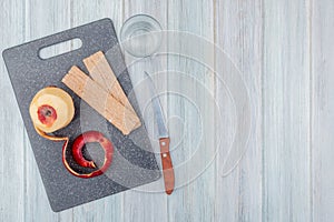 Top view of red apple with shell and cookies on cutting board with knife and glass of water on wooden background with copy space