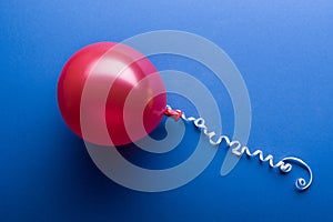 Top view of red balloon with white streamer on blue background.