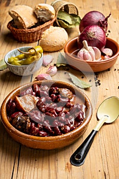 Top view of red bean stew on rustic wooden table with spoon, green chillies, garlic, onions, bay leaf