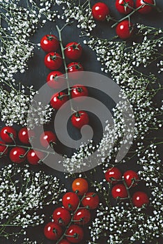 top view of red cherry tomatoes and white flowers on black