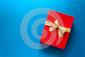 Top view on red Christmas gift box decorated with ribbon on blue paper background.