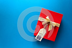 Top view on red Christmas gift box decorated with ribbon on blue paper background. New Year, holidays and celebration decorations