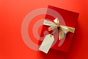 Top view on red Christmas gift box decorated with ribbon on red paper background. New Year, holidays and celebration decorations c
