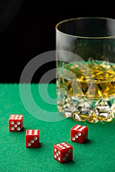 Top view of red dice on green baize with glass of whiskey, defocused, black background