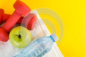 Top view of red dumbbells, green apple and fresh water bottle with dew on white towel and yellow space