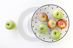 Top view of Red and green apples in white plate with black triangles pattern and green apple on white background