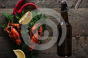 Top view of red lobsters, lemon slices, dill, pepper and bottle with beer on wooden surface.