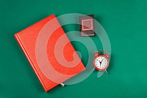 Top view of a red Notepad, a small book and a small alarm clock, on a green background. Romance. Concept of time and