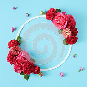 Top view of red roses with green leaves and white frame on pastel blue background.