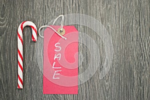 Top view of a red sale tag with a candy cane on a wooden surface