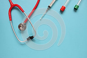 Top view of red stetoscope, syringe, and ampoules on blue background. Medicine concept.