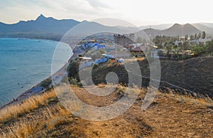 top view of resort town on shore of Black Sea bay among mountains and rocks, blue emerald water, summer, dry yellow grass